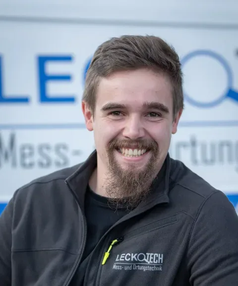 Techniker von LECKOTECH lächelt für ein Porträtfoto vor dem Firmenbanner