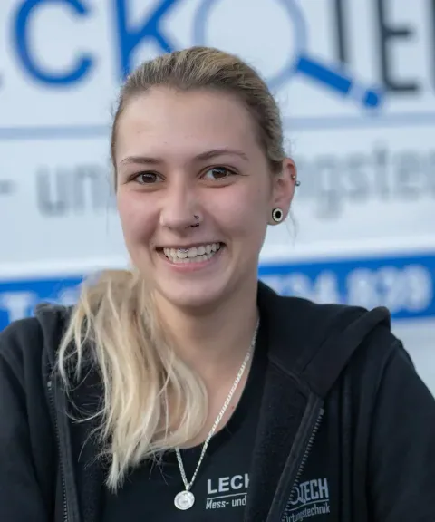 Mitarbeiterin von LECKOTECH lächelt für ein Teamporträt vor dem Firmenbanner