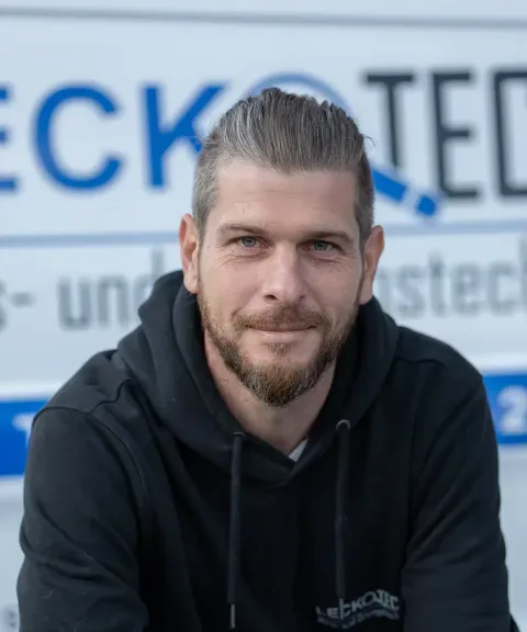 Techniker von LECKOTECH blickt lächelnd in die Kamera vor dem Firmenbanner
