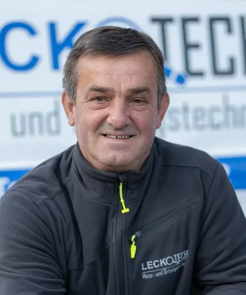 Mitarbeiter von LECKOTECH lächelt für ein Porträtfoto vor dem Firmenschriftzug