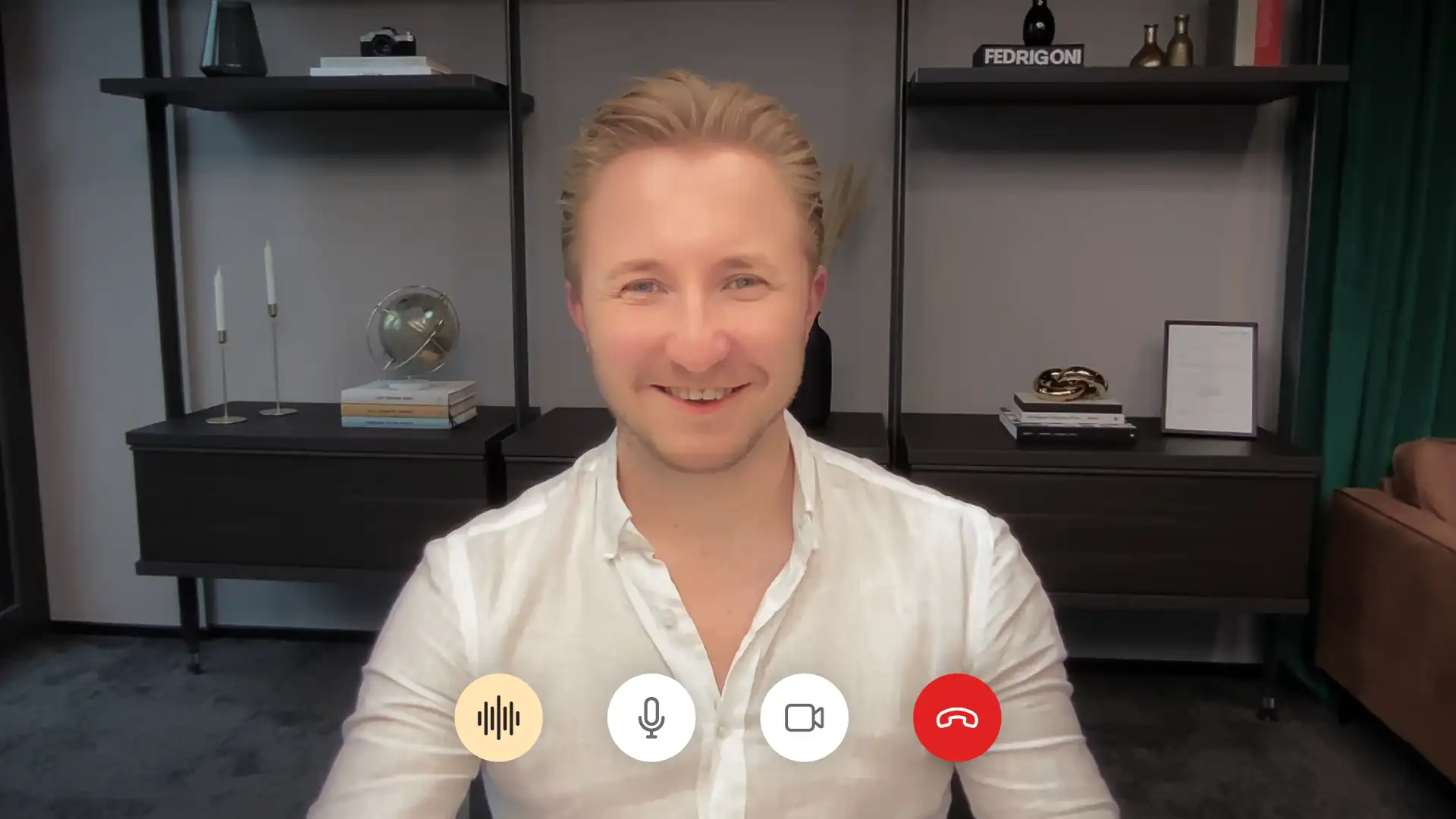 Sebastian Klein von Martin&Klein lächelt im Videocall in die Kamera, hinter ihm ein Regal