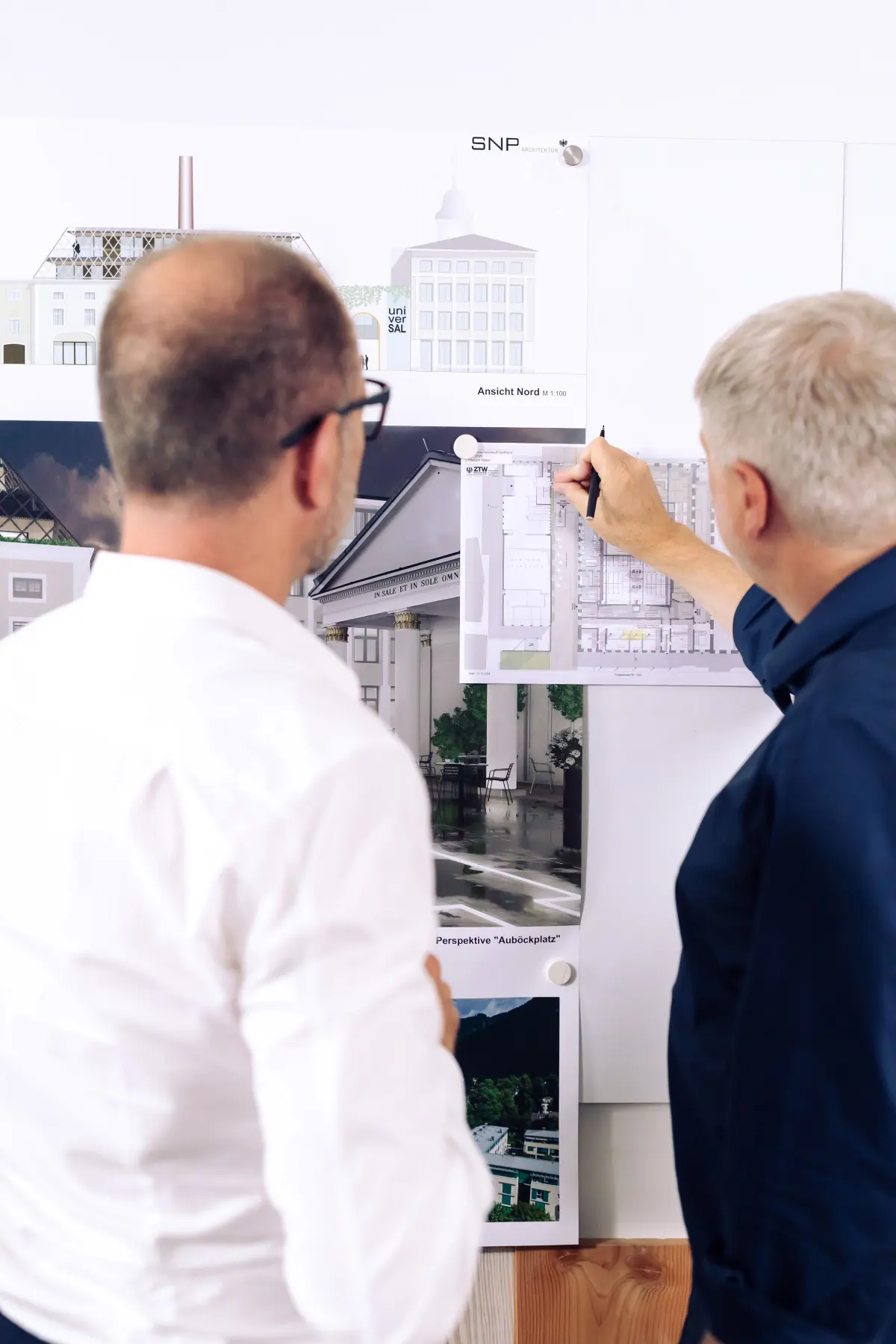 Zwei Planer besprechen vor der Projektwand von SNP Architektur Ansichten und Grundrisse