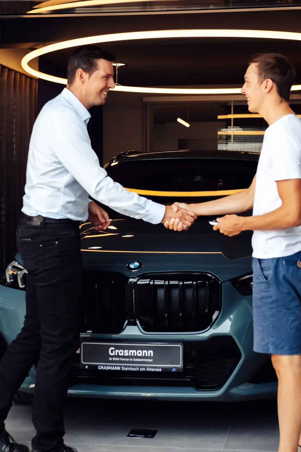 Handschlag bei der Fahrzeugübergabe vor einem neuen BMW im Showroom von Autohaus Grasmann