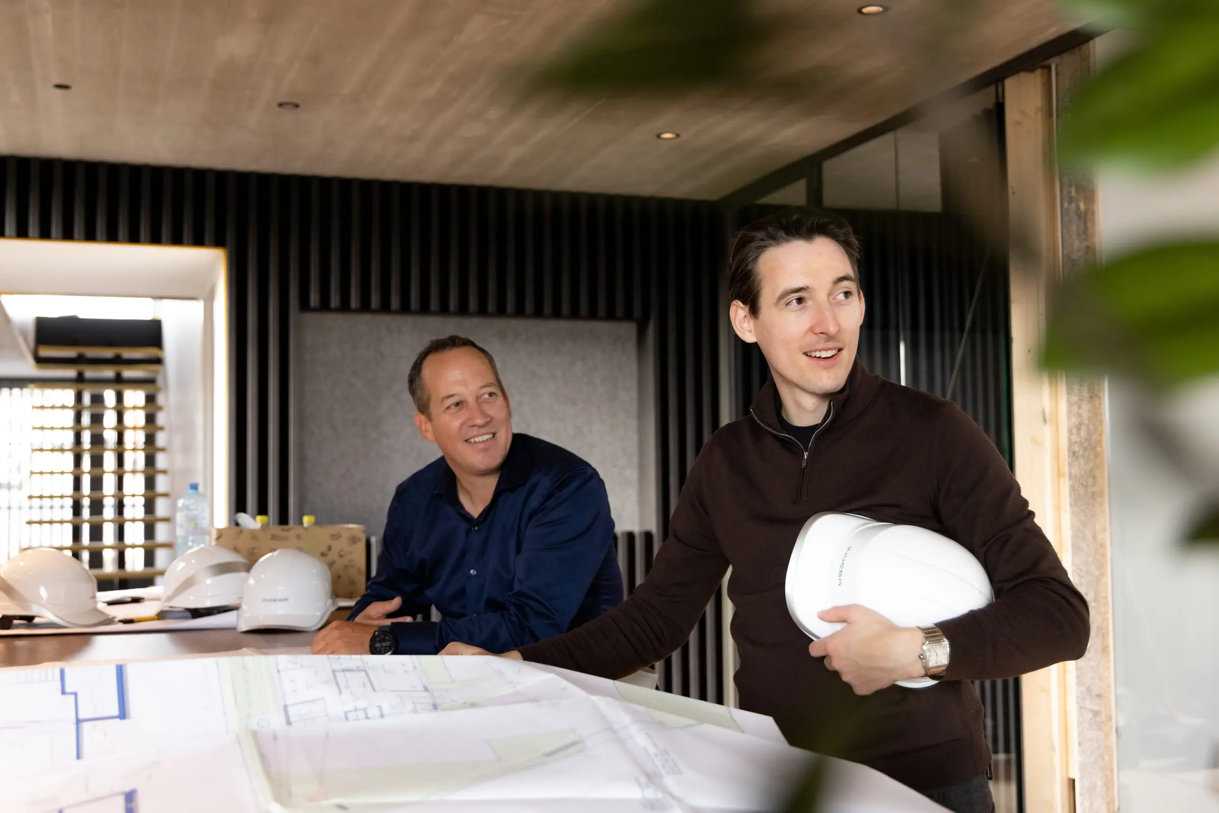 Christoph Martin bespricht mit einem Kunden von Ingeba Baupläne, auf dem Tisch liegen Bauhelme