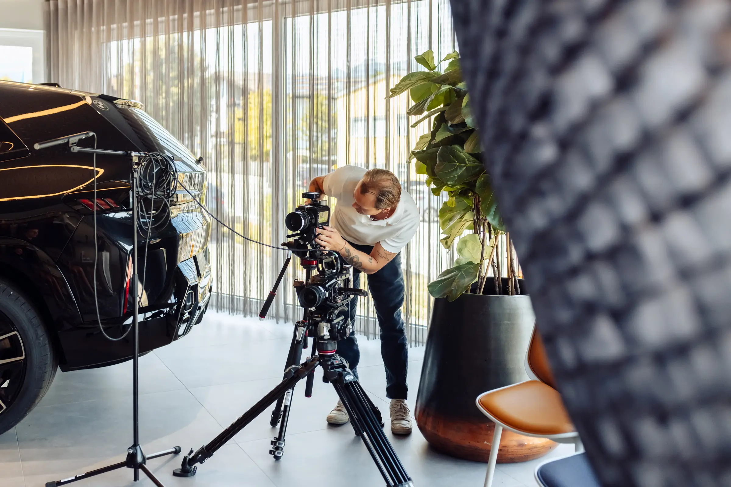 Kameramann von Martin&Klein richtet beim Videodreh im Showroom neben einem dunklen SUV die Kamera ein