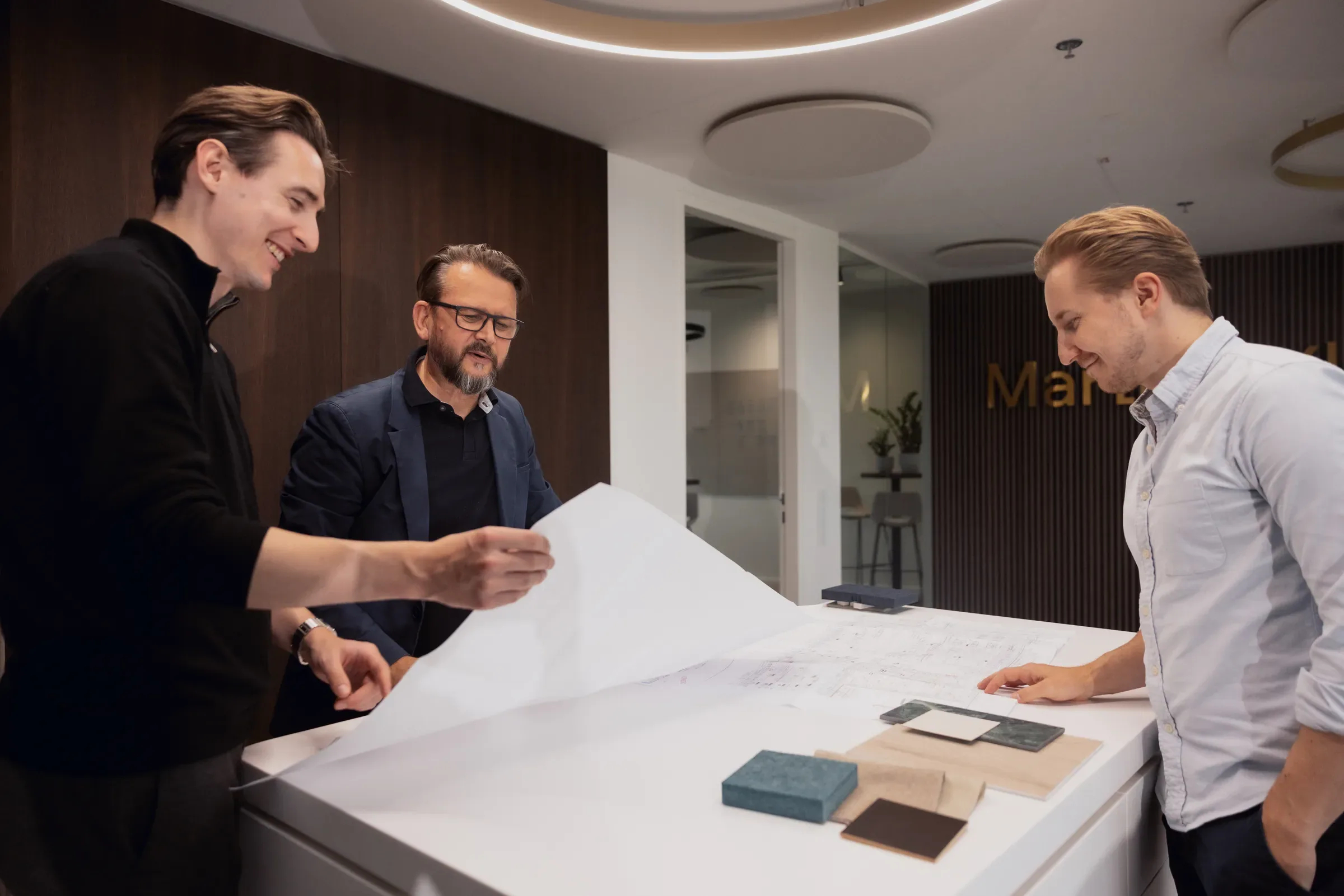 Christoph Martin bespricht mit einem Kunden und einem Kollegen Pläne und Materialmuster im Martin&Klein-Büro
