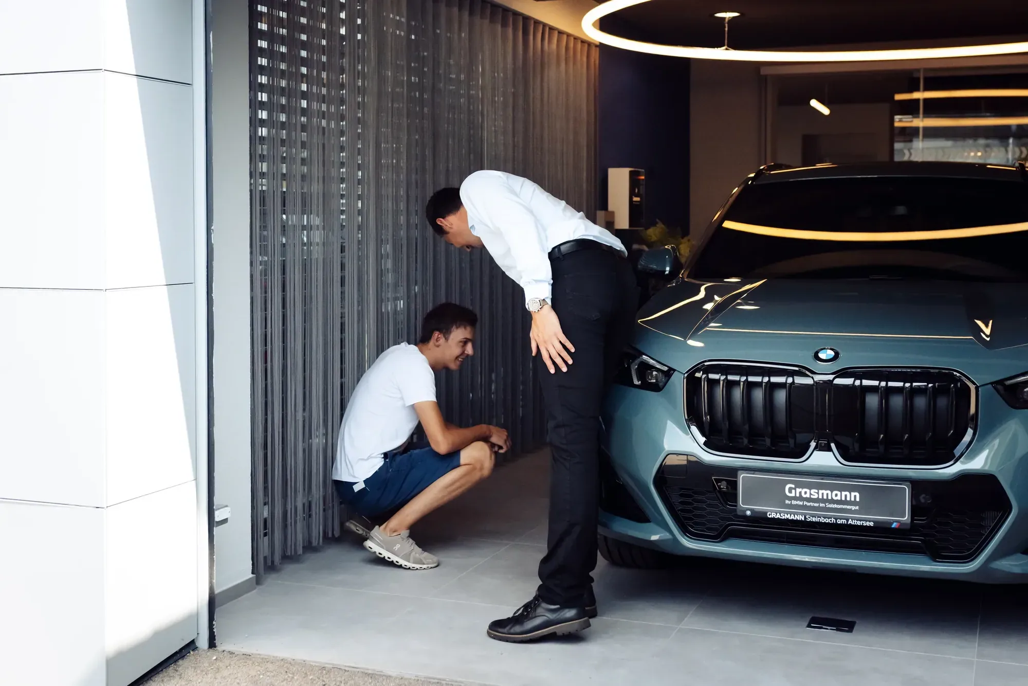 Zwei Männer inspizieren einen türkisblauen BMW in einer modernen Tiefgarage