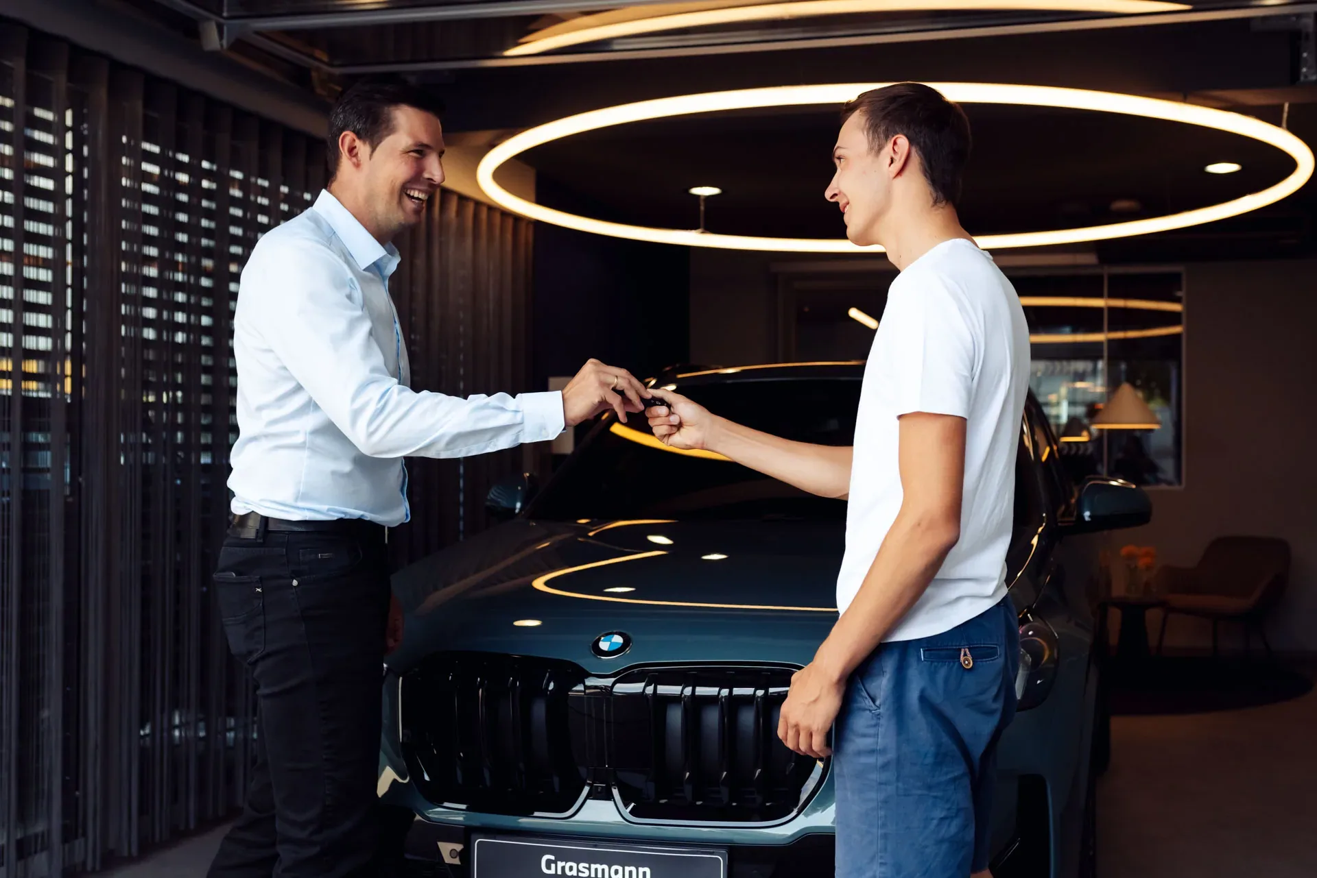 Schlüsselübergabe vor einem neuen BMW im Showroom