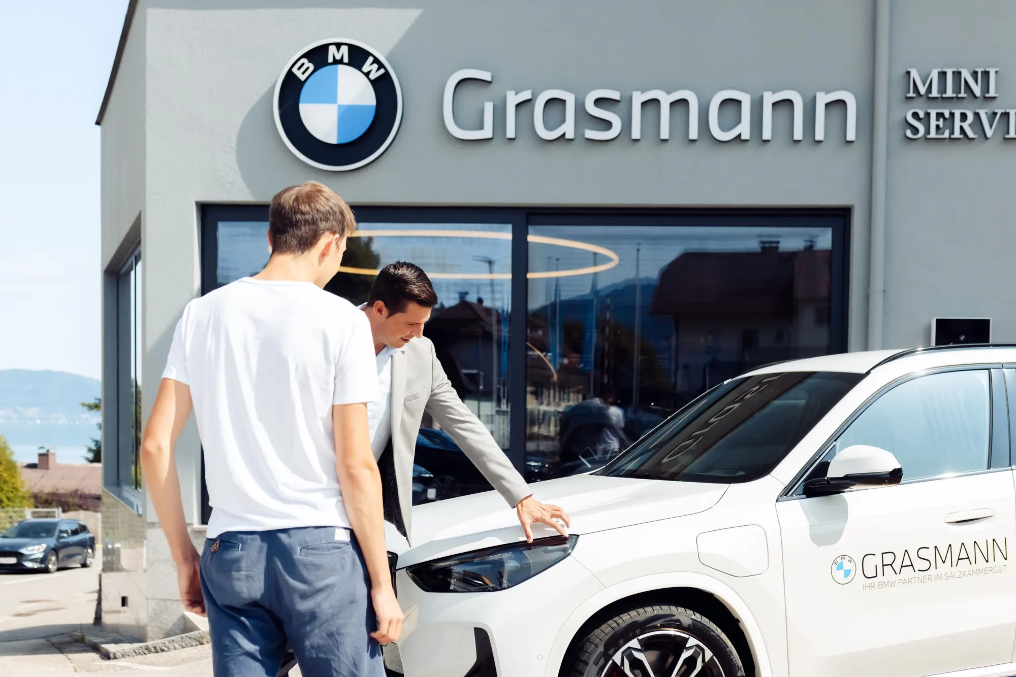 Zwei Männer begutachten einen weißen BMW vor dem Autohaus Grasmann