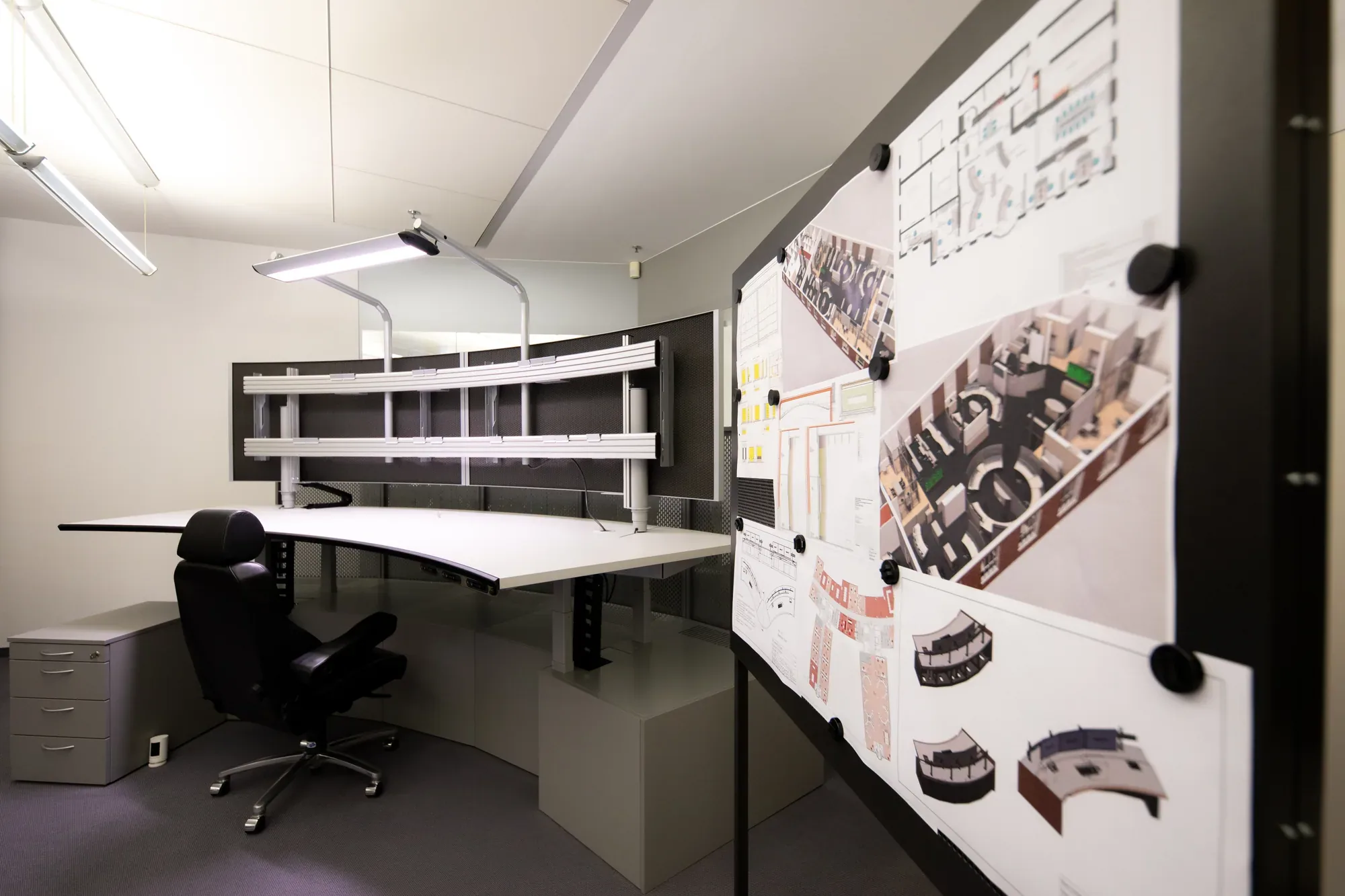 Leittisch mit Monitortragsystem, daneben eine Planwand mit 3D-Entwürfen