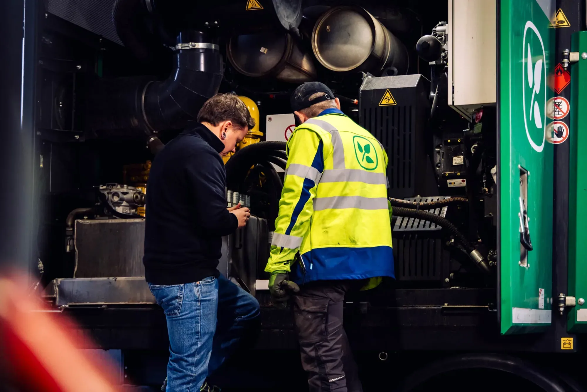 Servicetechniker und Kunde besprechen sich am offenen Motorraum einer Maschine