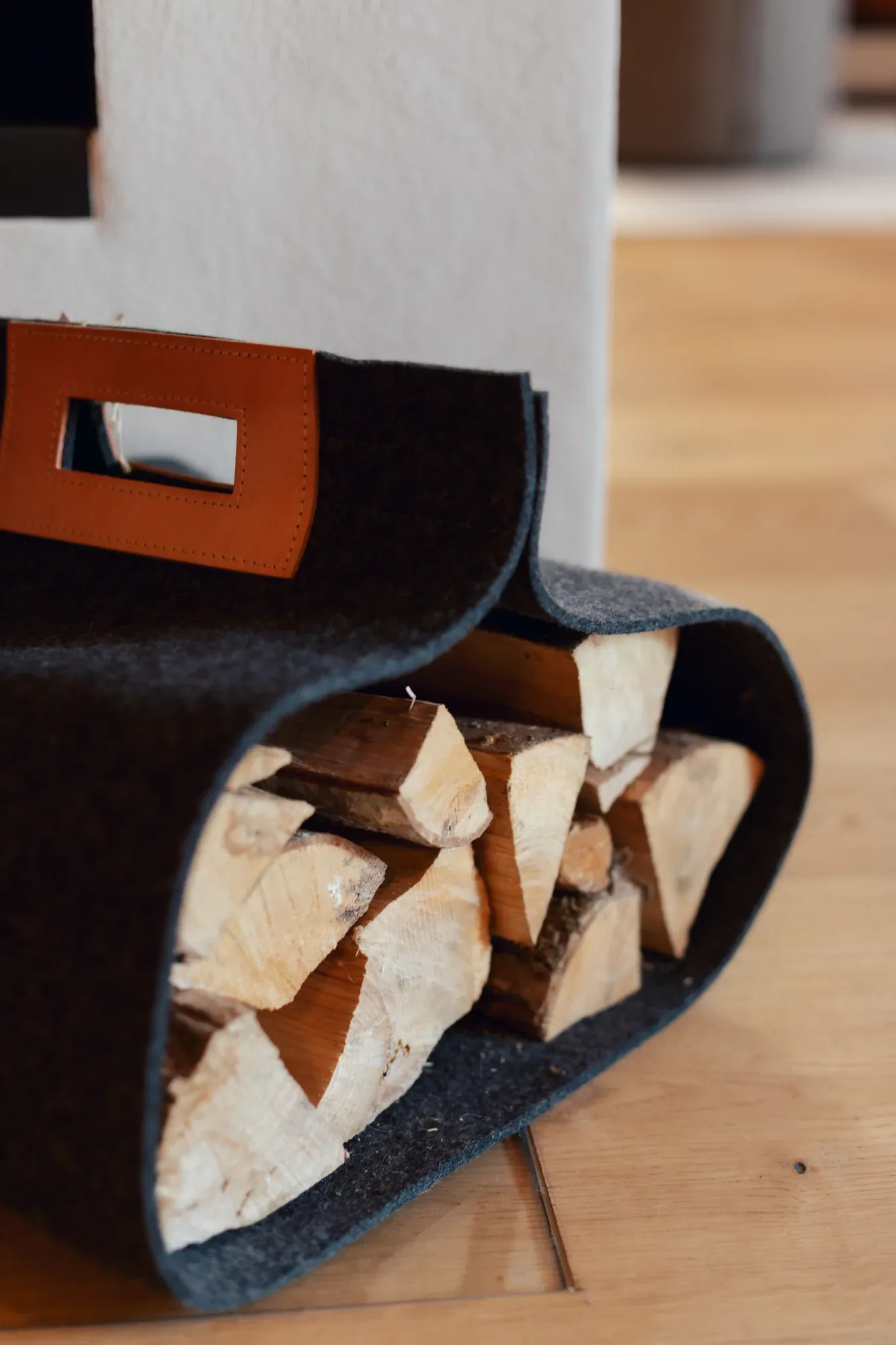 Kaminholztasche aus dunklem Filz mit Lederschlaufe, gefüllt mit Holzscheiten