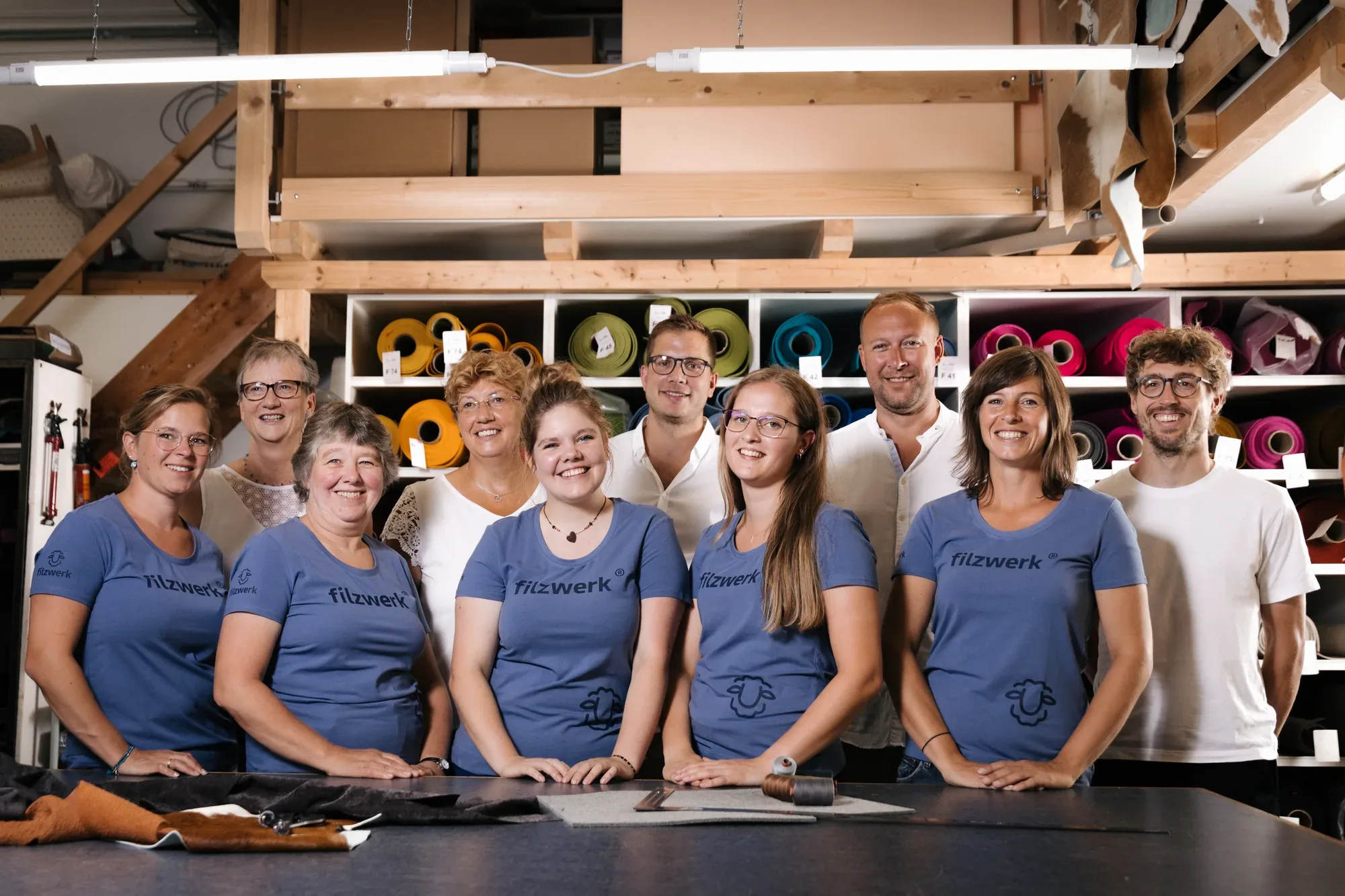 Das Team von Filzwerk in blauen Shirts vor dem Regal mit Wollfilzrollen