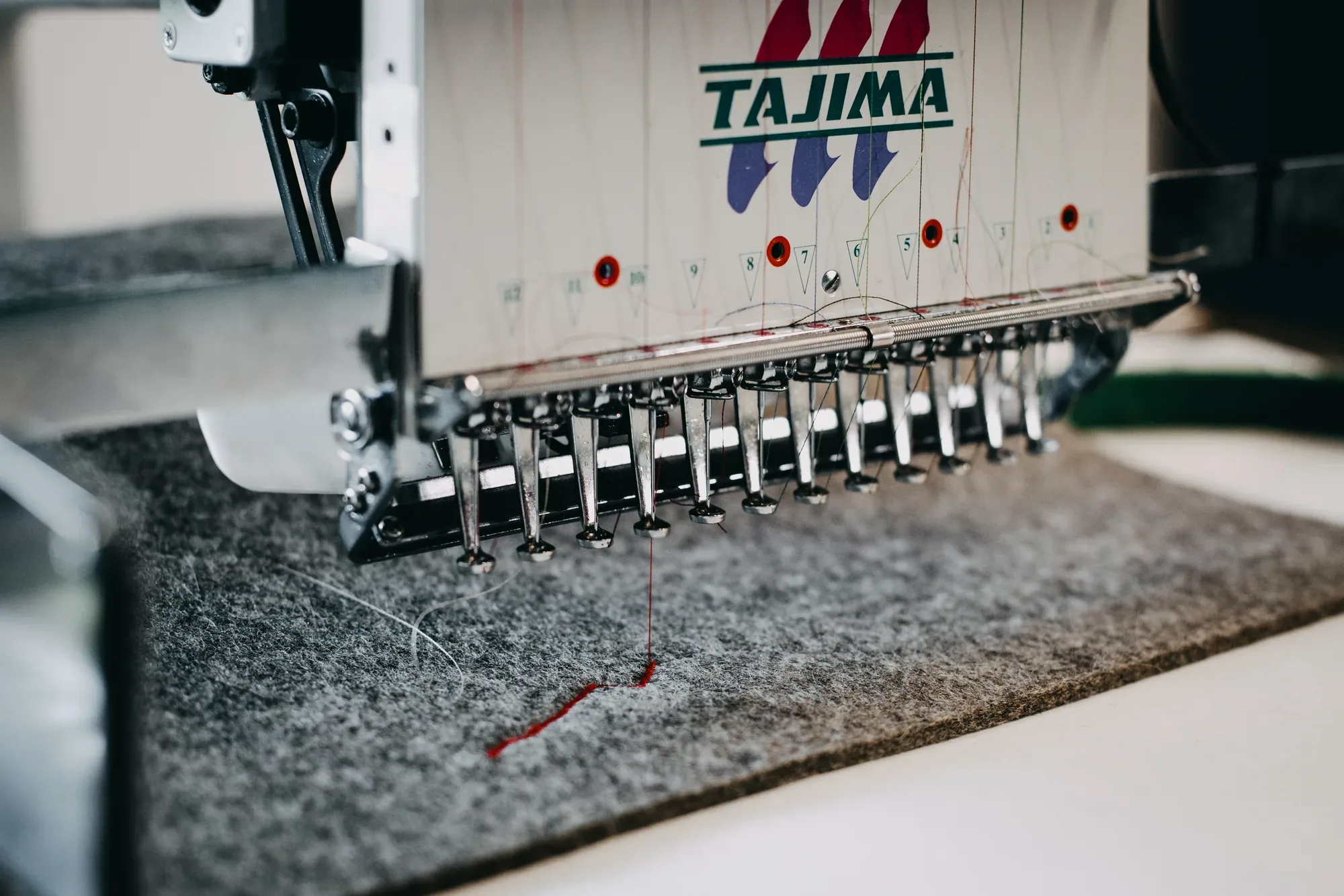 Stickmaschine bestickt grauen Wollfilz in der Werkstatt