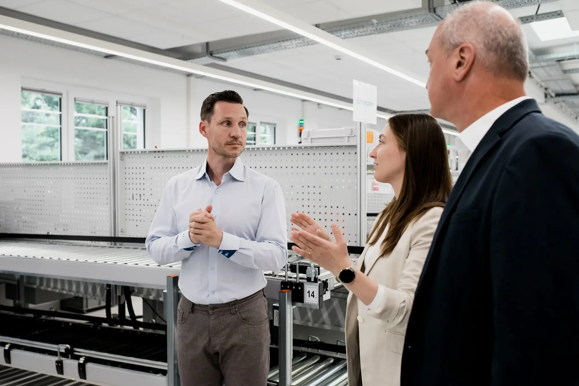 Gespräch zu dritt in einer hellen Produktionshalle mit Fertigungsstraße bei giefing.