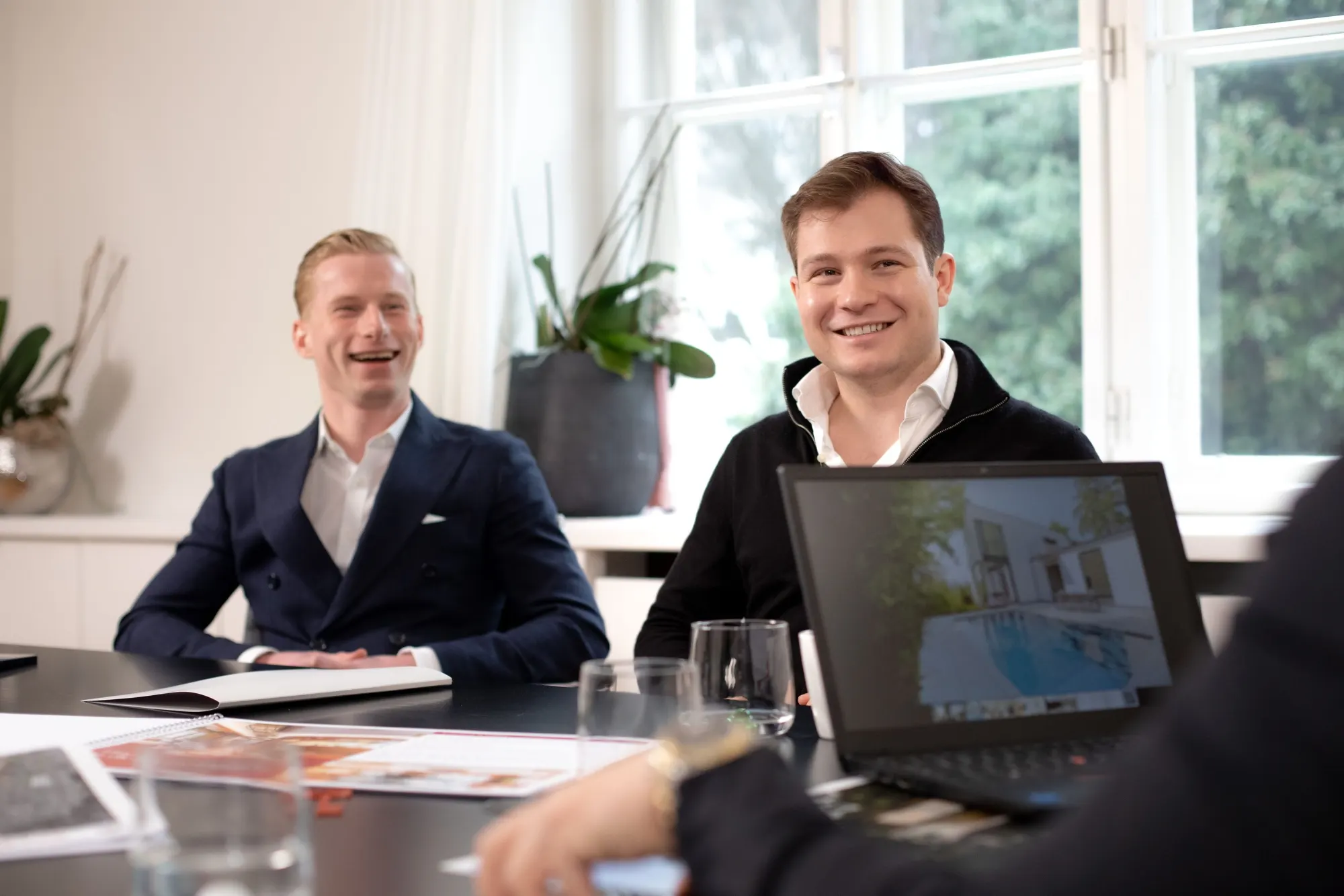 Zwei Männer von Greisberger Immobilien lachen in einer Besprechung am Tisch