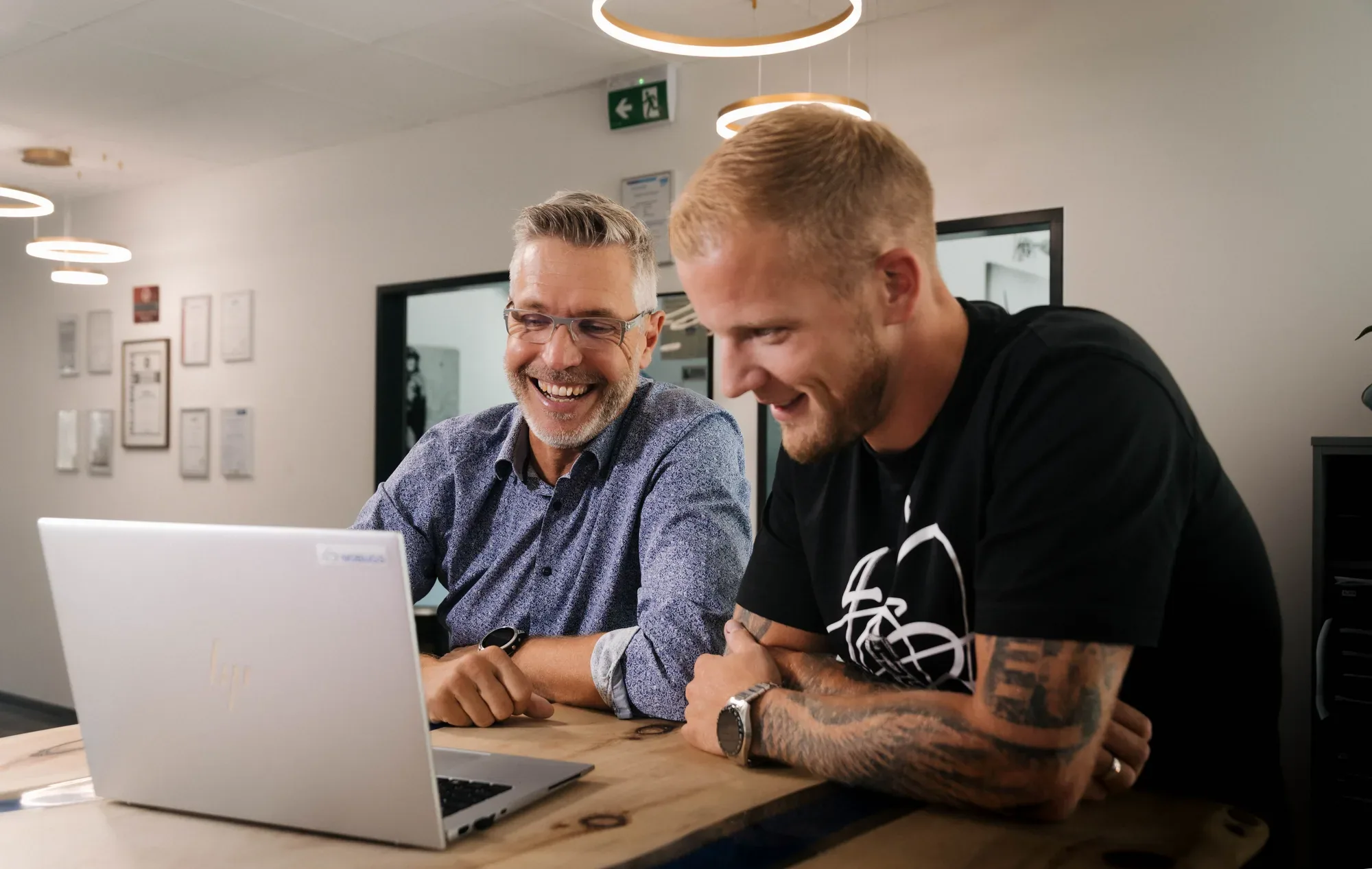 Vinzenz Wolf und ein Kunde lachen gemeinsam vor einem Laptop