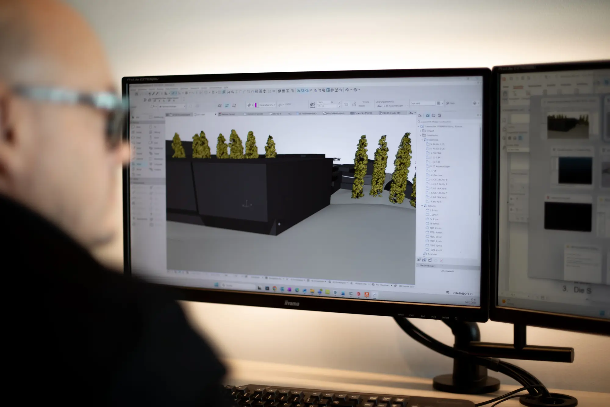 Planer arbeitet am 3D-Modell eines Gebäudes auf zwei Bildschirmen