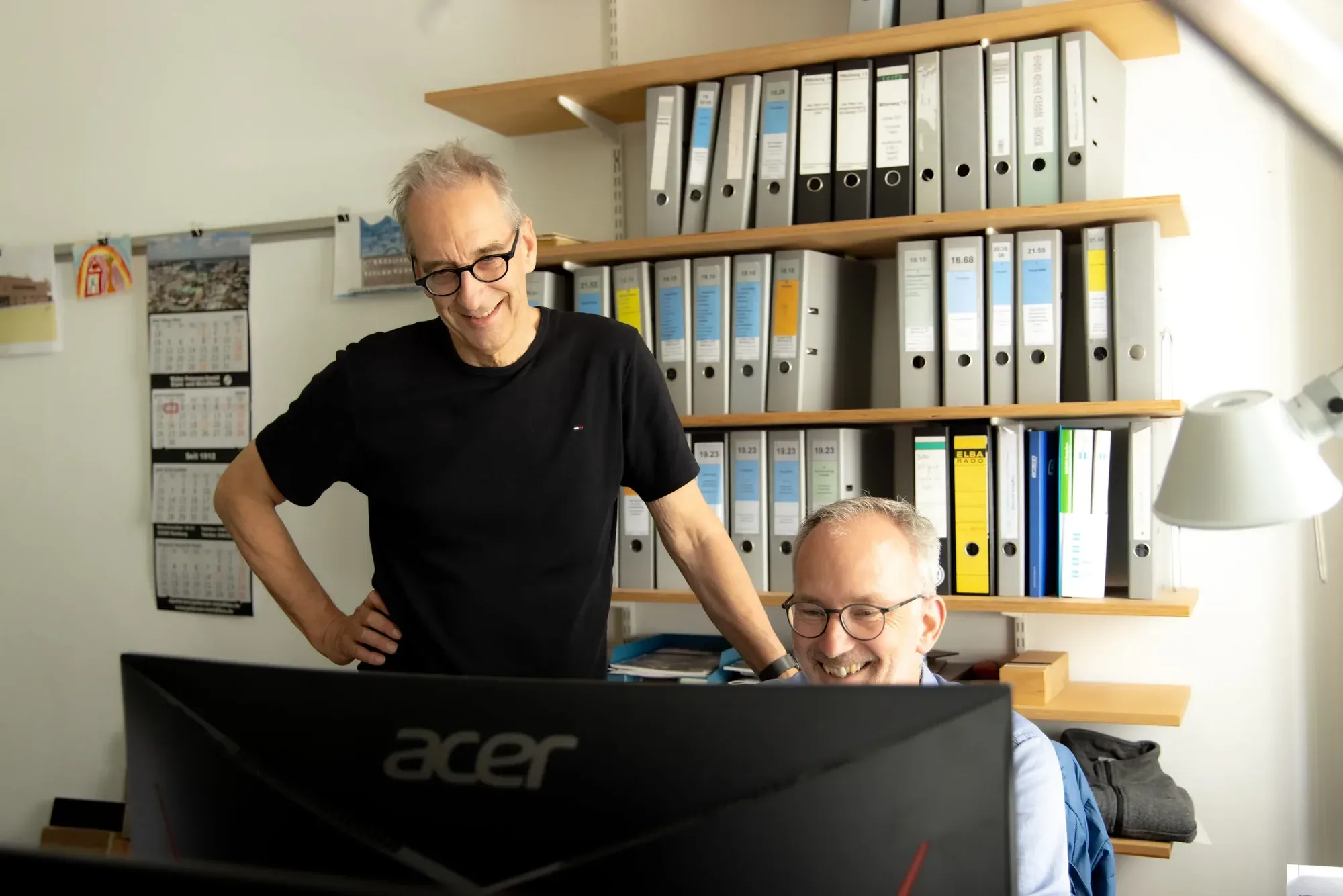 Zwei Architekten von Knaack & Prell besprechen lachend einen Entwurf am Bildschirm im Büro