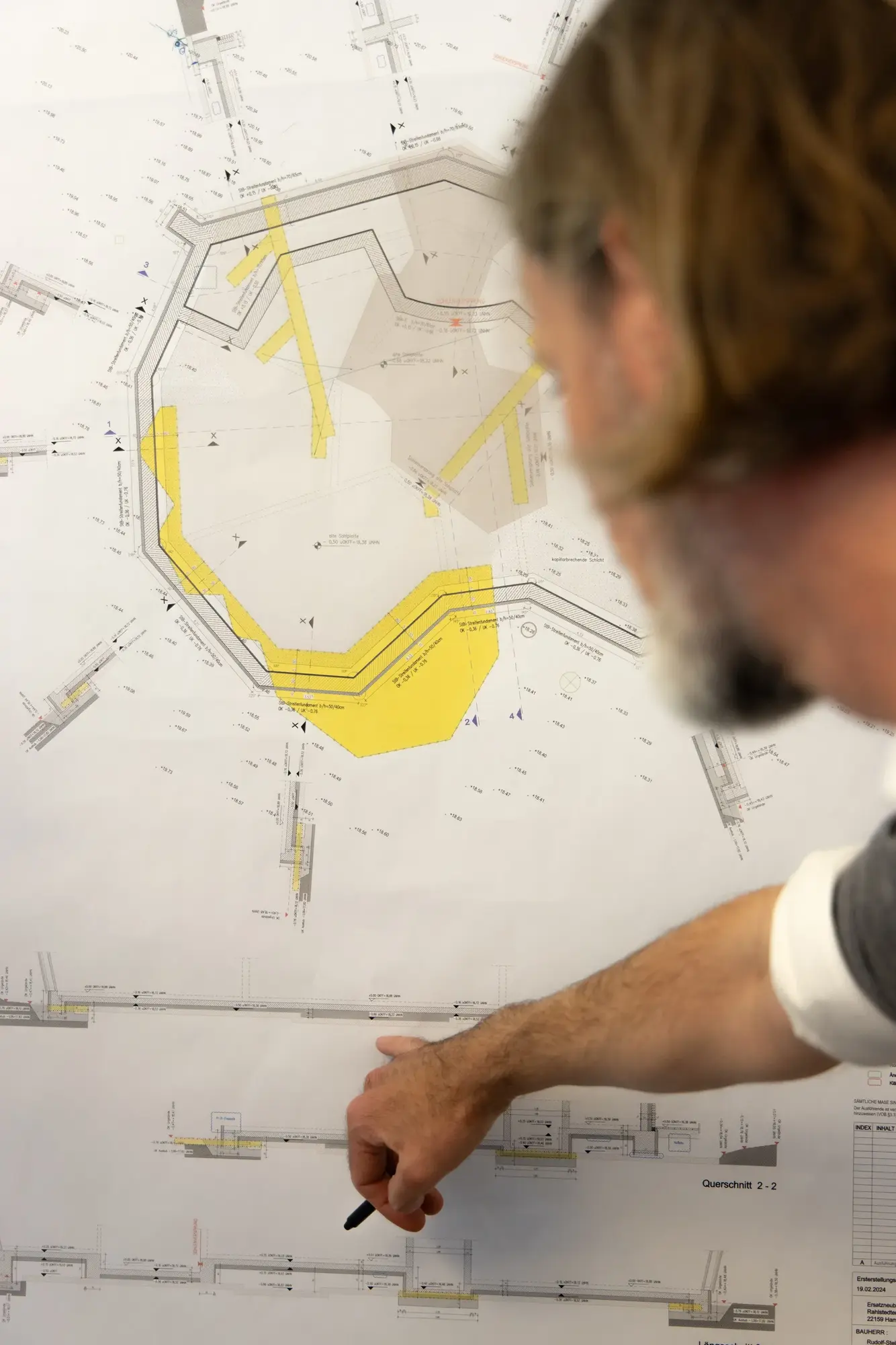 Ein Architekt markiert auf einem Lageplan an der Wand eine gelbe Fläche