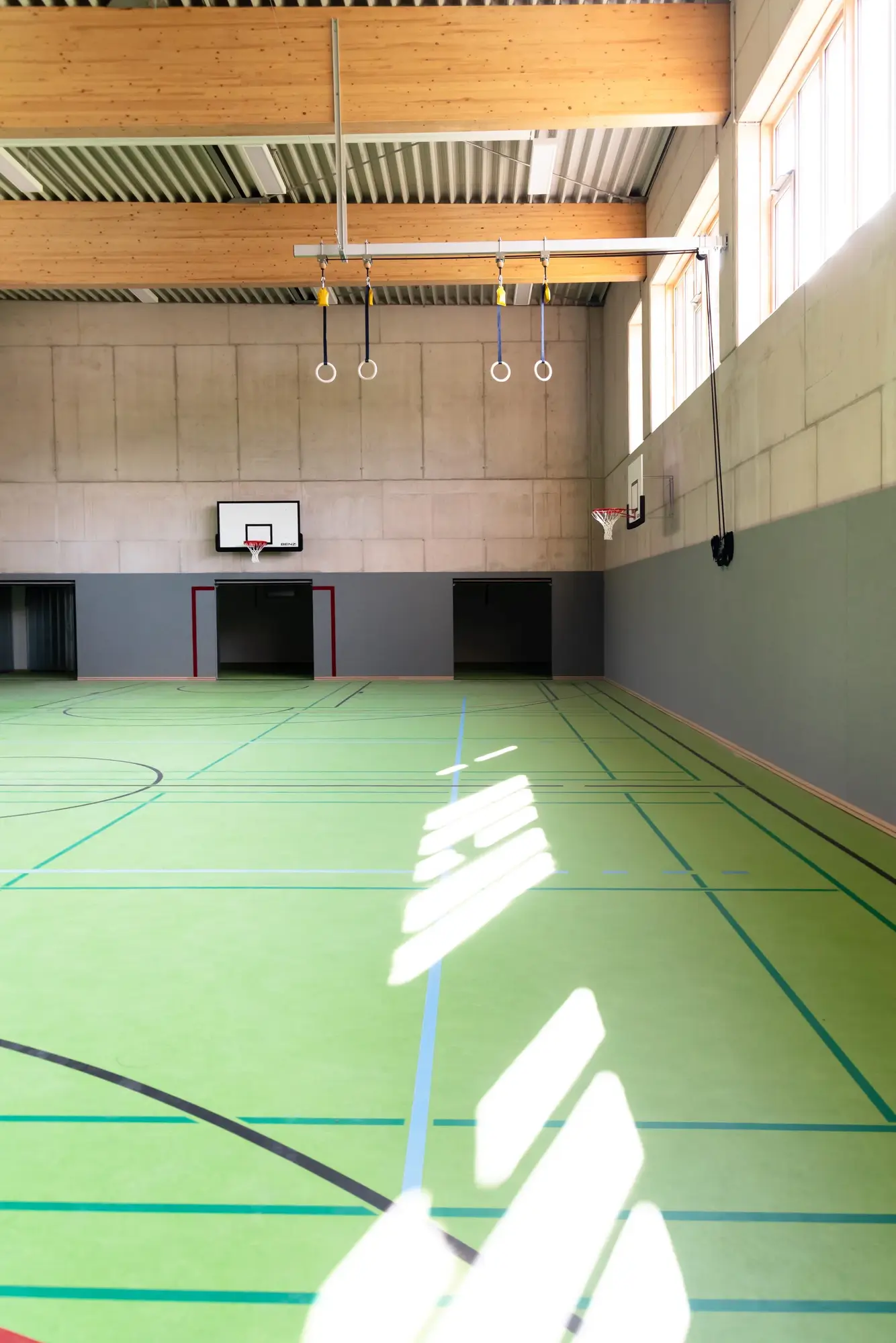 Sonnenlicht fällt durch die Fensterreihe auf den grünen Boden einer Sporthalle