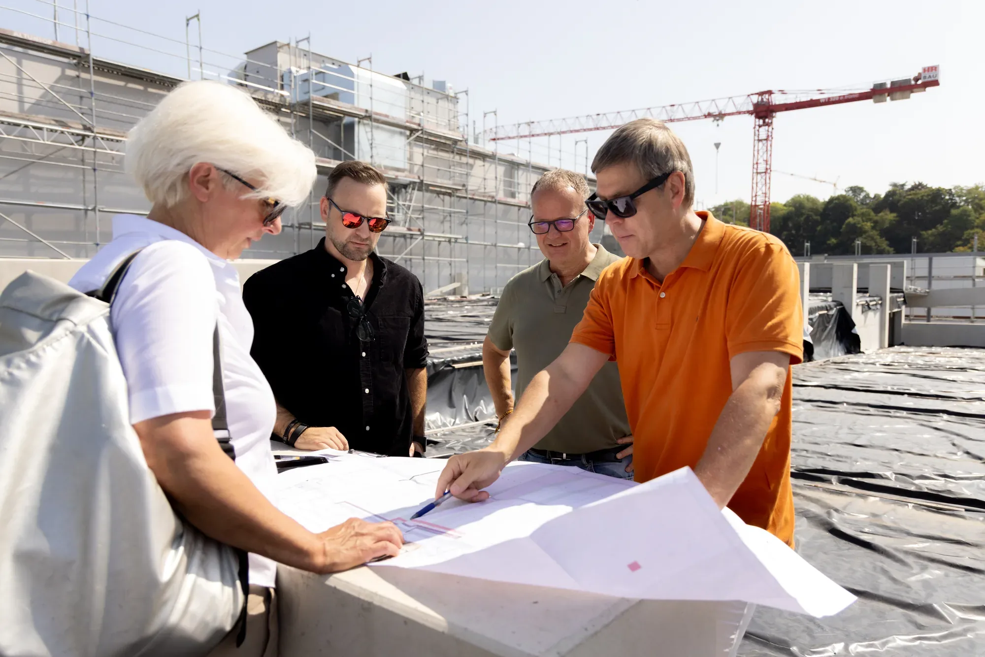Planer und Bauherren besprechen Pläne auf der Baustelle, im Hintergrund ein Kran