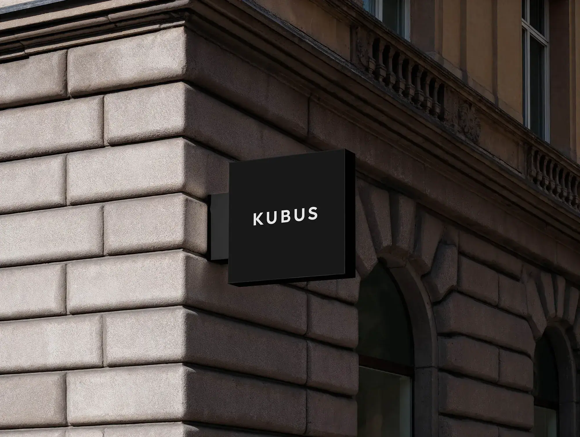 Schwarzes KUBUS-Ausleger-Schild an einer Steinfassade