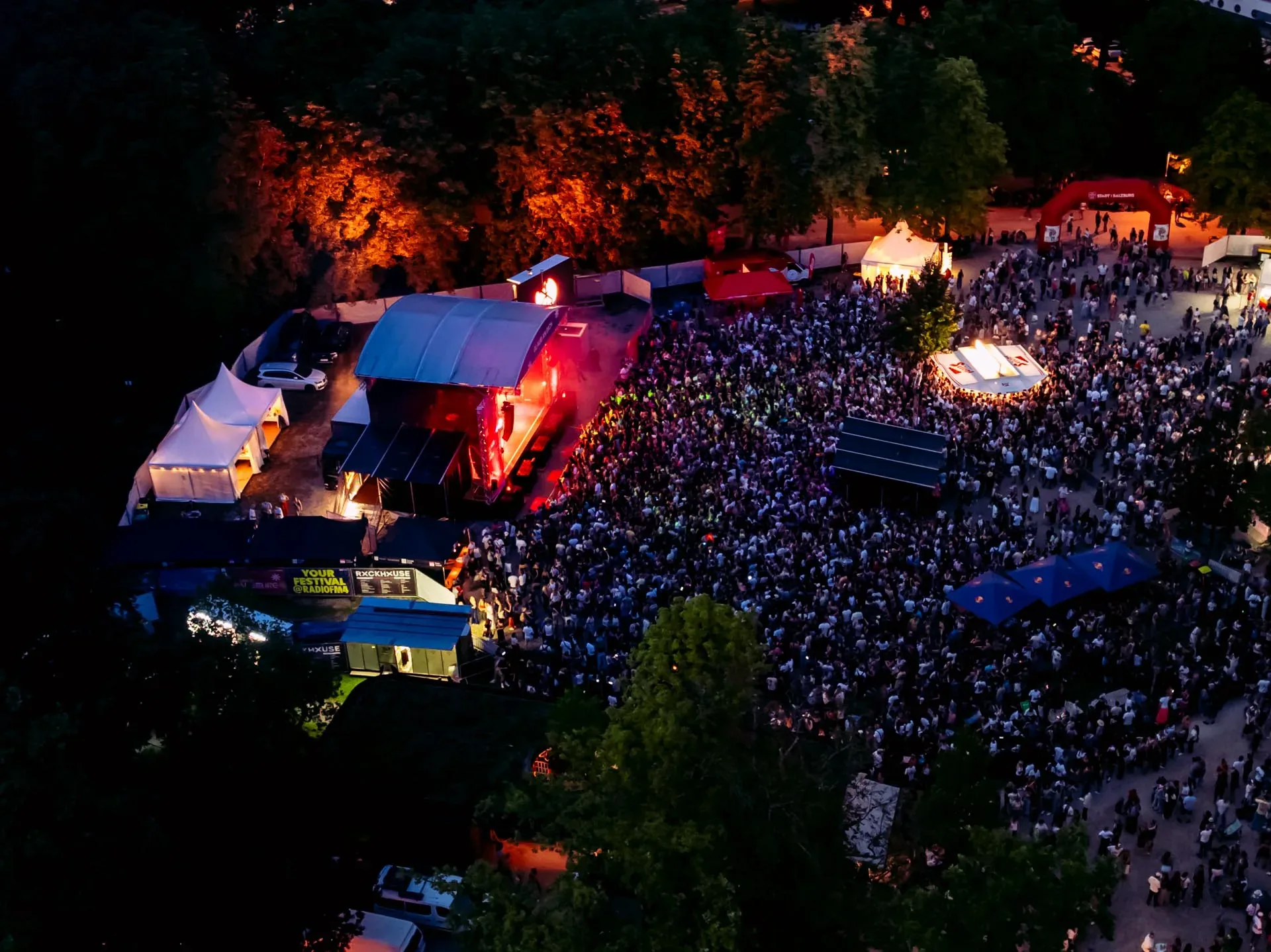 Luftaufnahme des Volksgartens bei Nacht: Bühne, Zelte und ein dicht gefülltes Festivalgelände