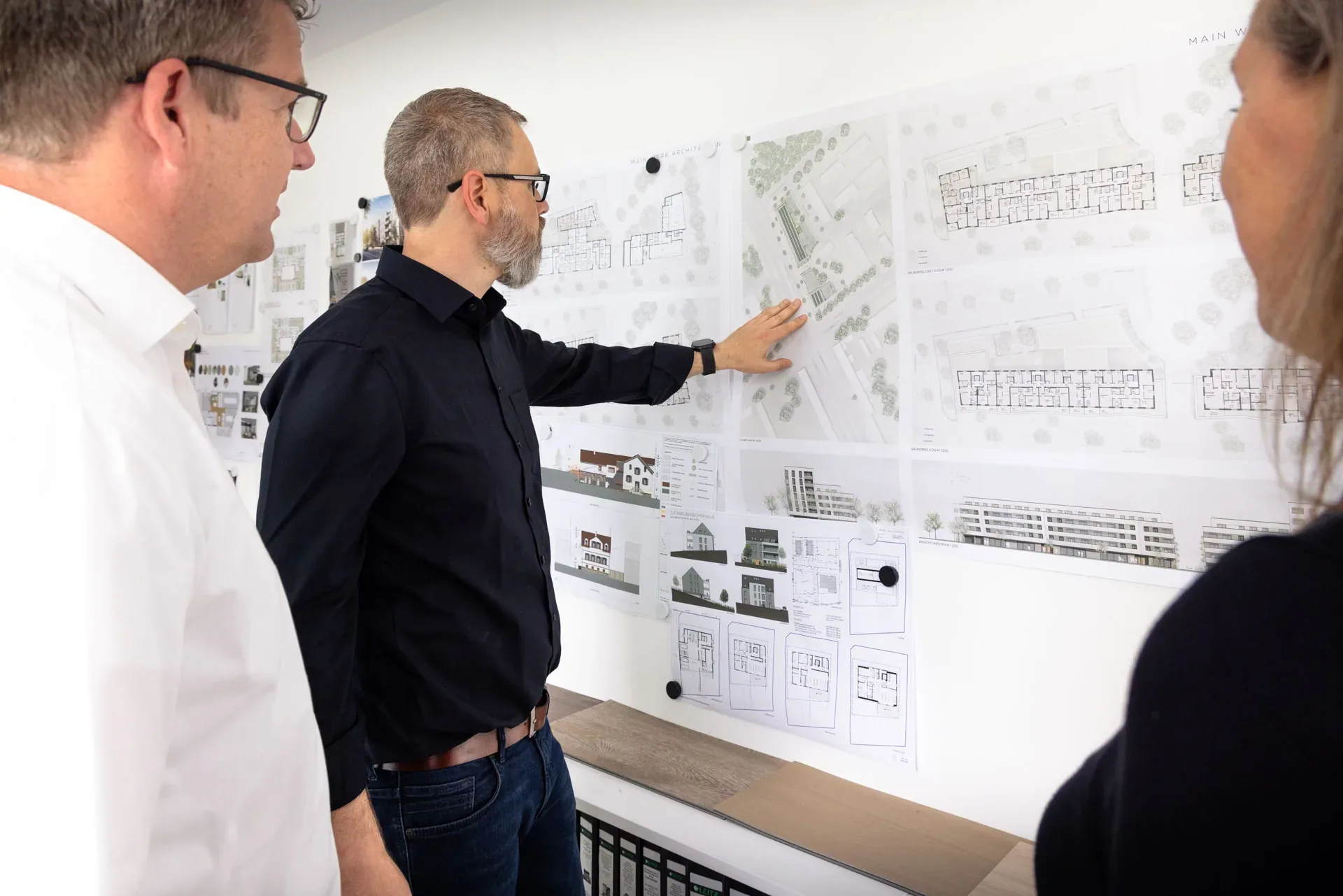 Architekt von Main Werk Architekten erklärt Kollegen an der Projektwand Pläne und Ansichten