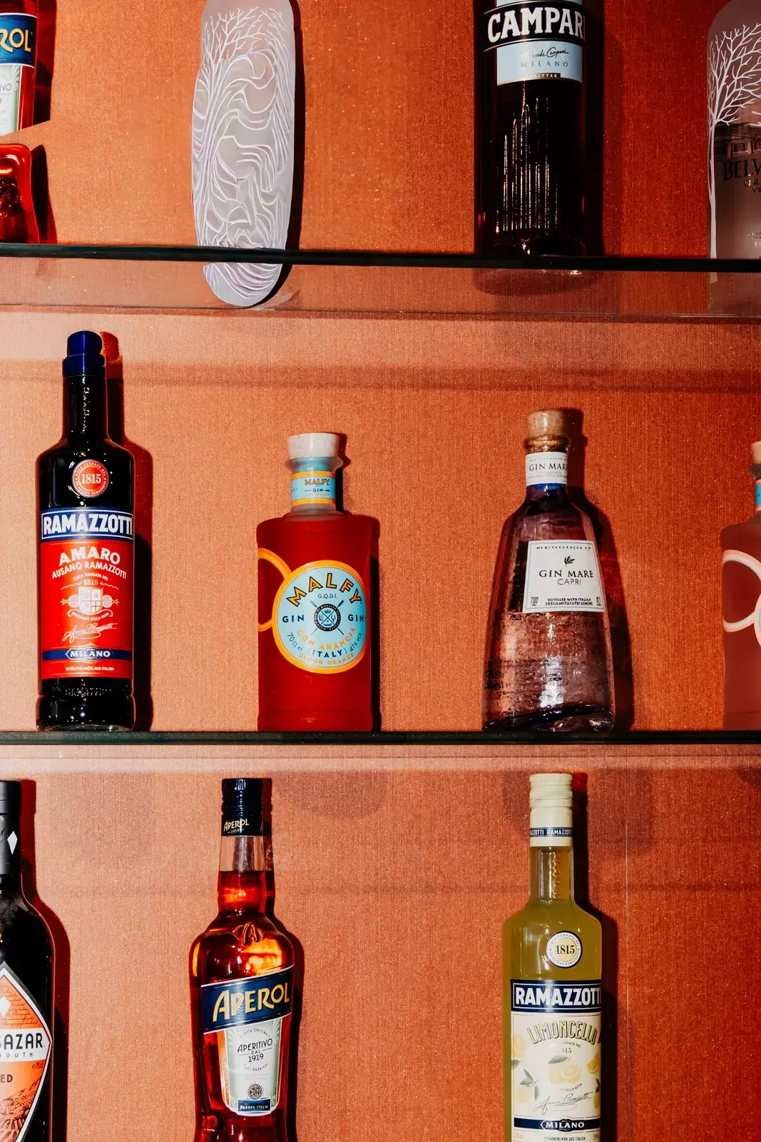 Aperitif-Flaschen auf Glasborden vor der orangefarbenen Wand