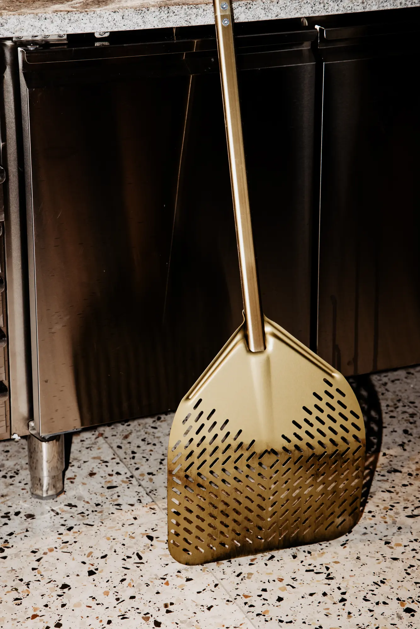 Goldene Pizzaschaufel lehnt am Terrazzo-Sockel der Küche