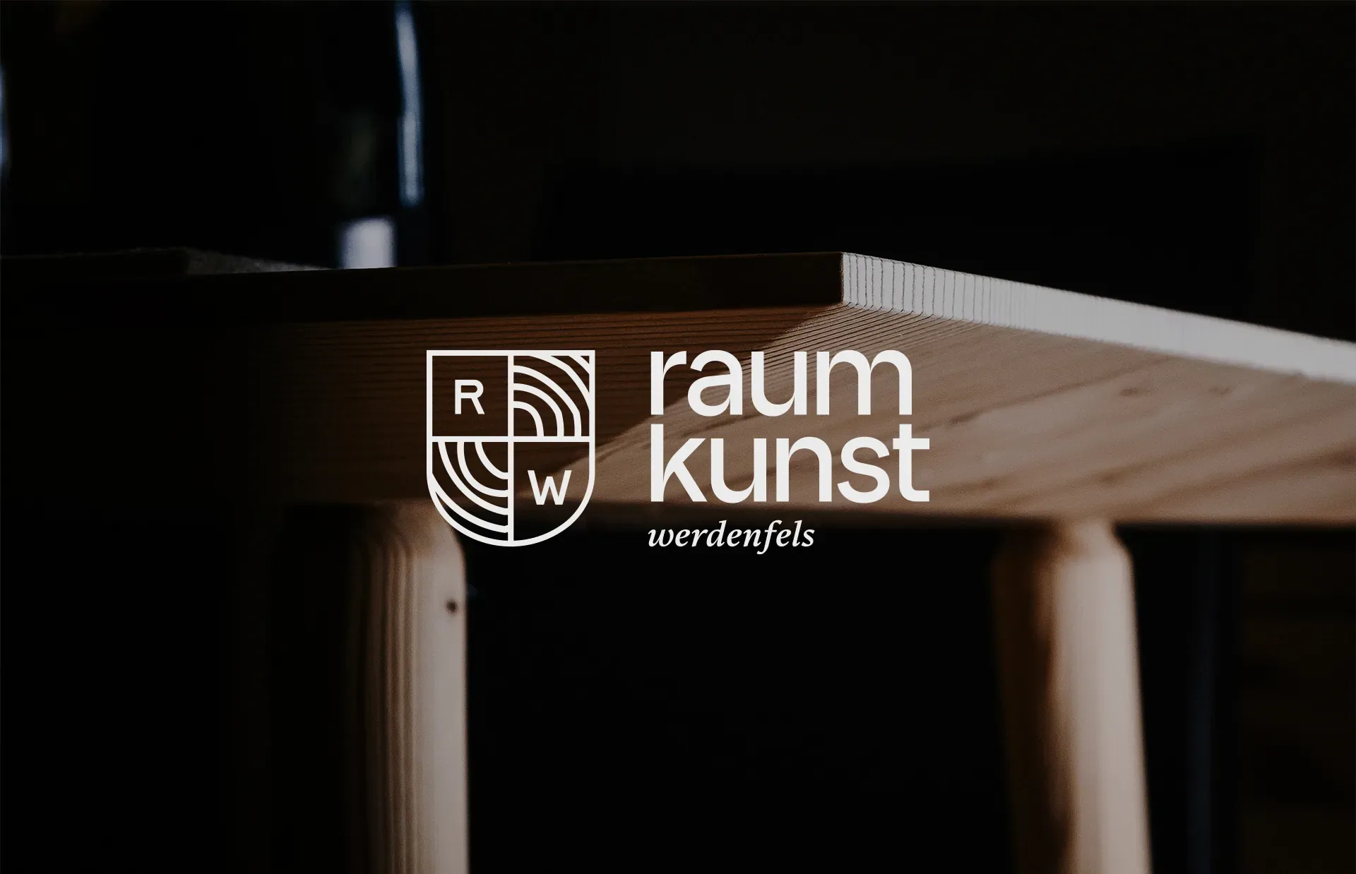 Logo von Raumkunst Werdenfels über einem Holztisch im Halbdunkel