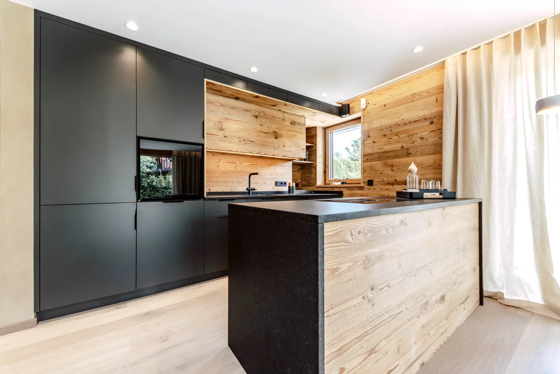 Küche mit schwarzen Fronten und Altholz in einer ausgebauten Wohnung