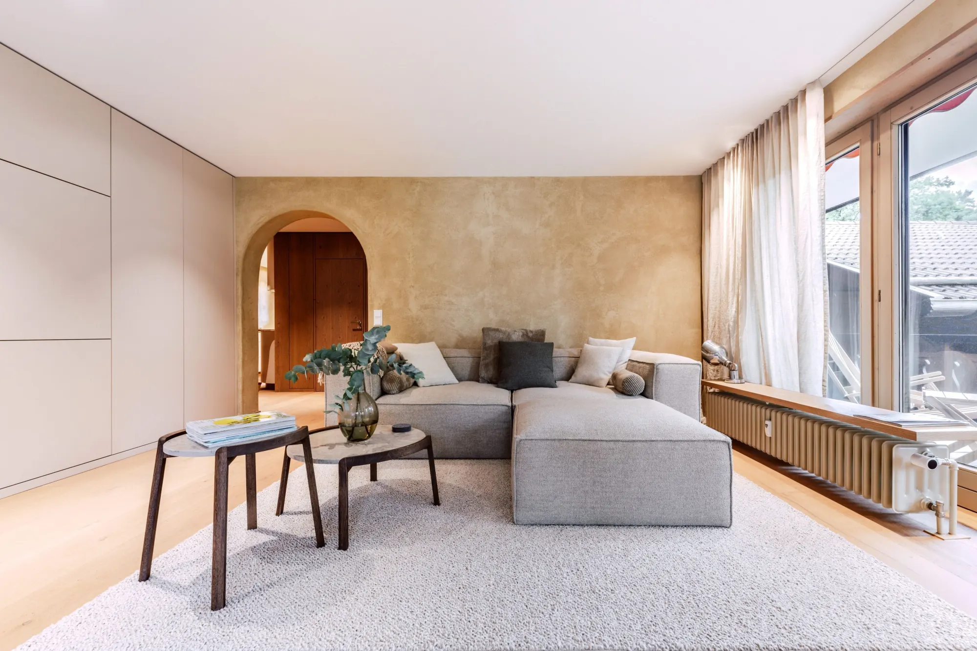 Helles Wohnzimmer von Raumkunst Werdenfels mit grauem Sofa, Rundbogen und Kalkputzwand