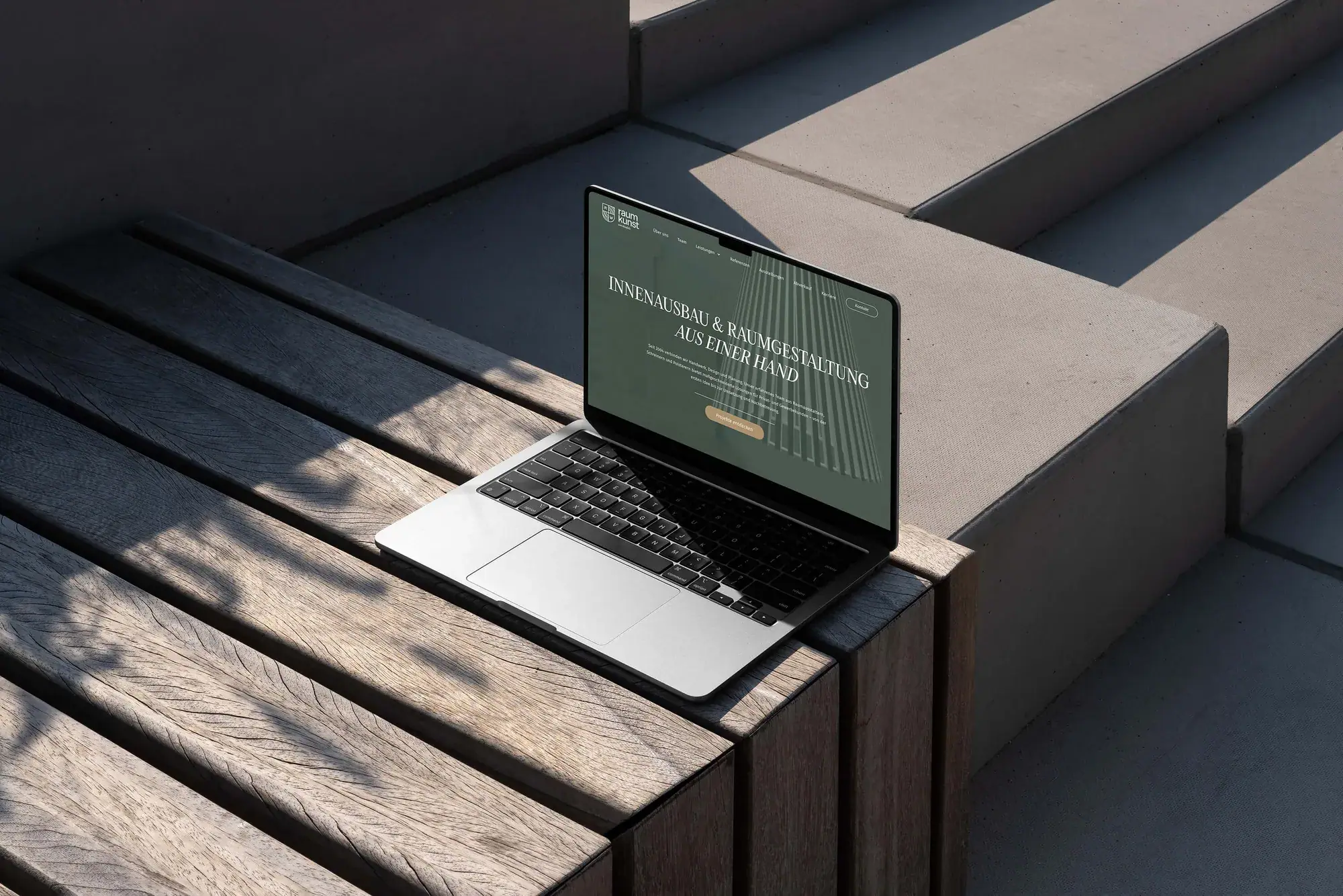 Laptop mit der Website von Raumkunst Werdenfels auf einer Holzbank im Freien