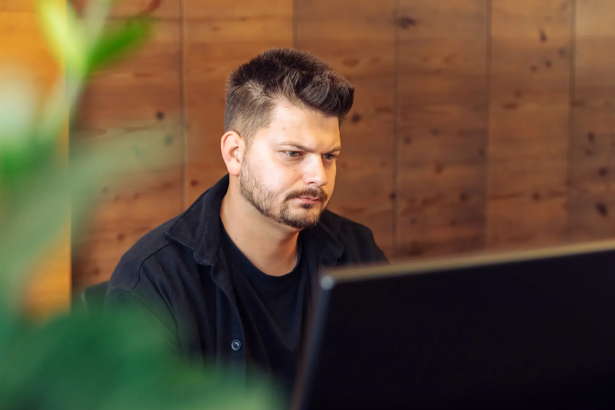 Mitarbeiter arbeitet konzentriert am Bildschirm, im Vordergrund eine Pflanze