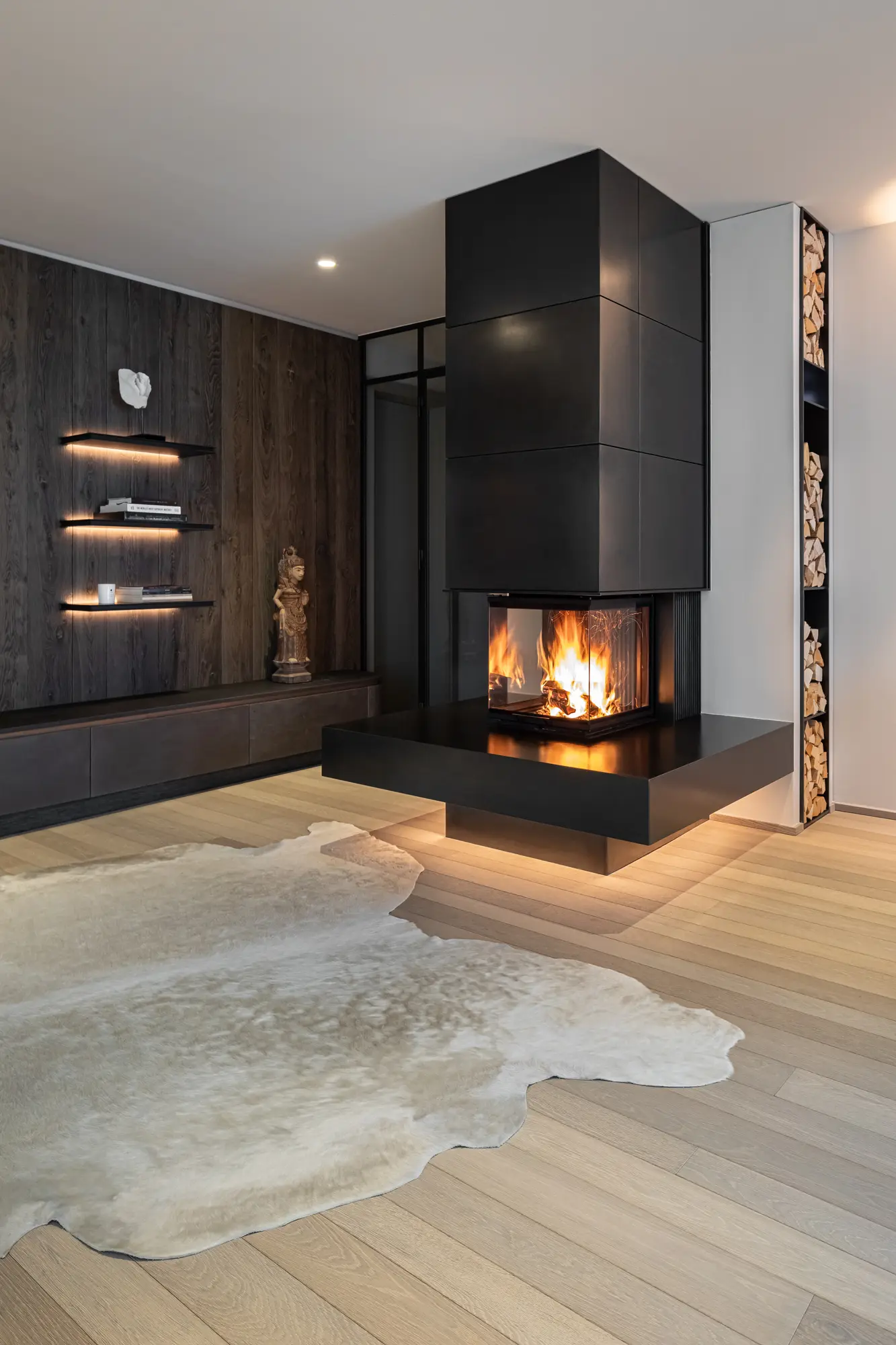 Freistehende schwarze Kaminsäule mit Holzfeuer in einem hellen Wohnraum