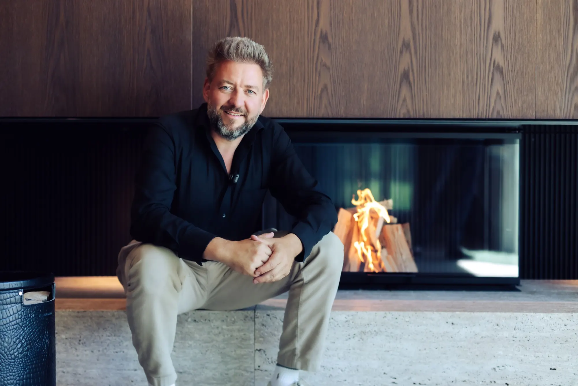 Stefan Schinharl sitzt lächelnd vor einem brennenden Designkamin im Showroom