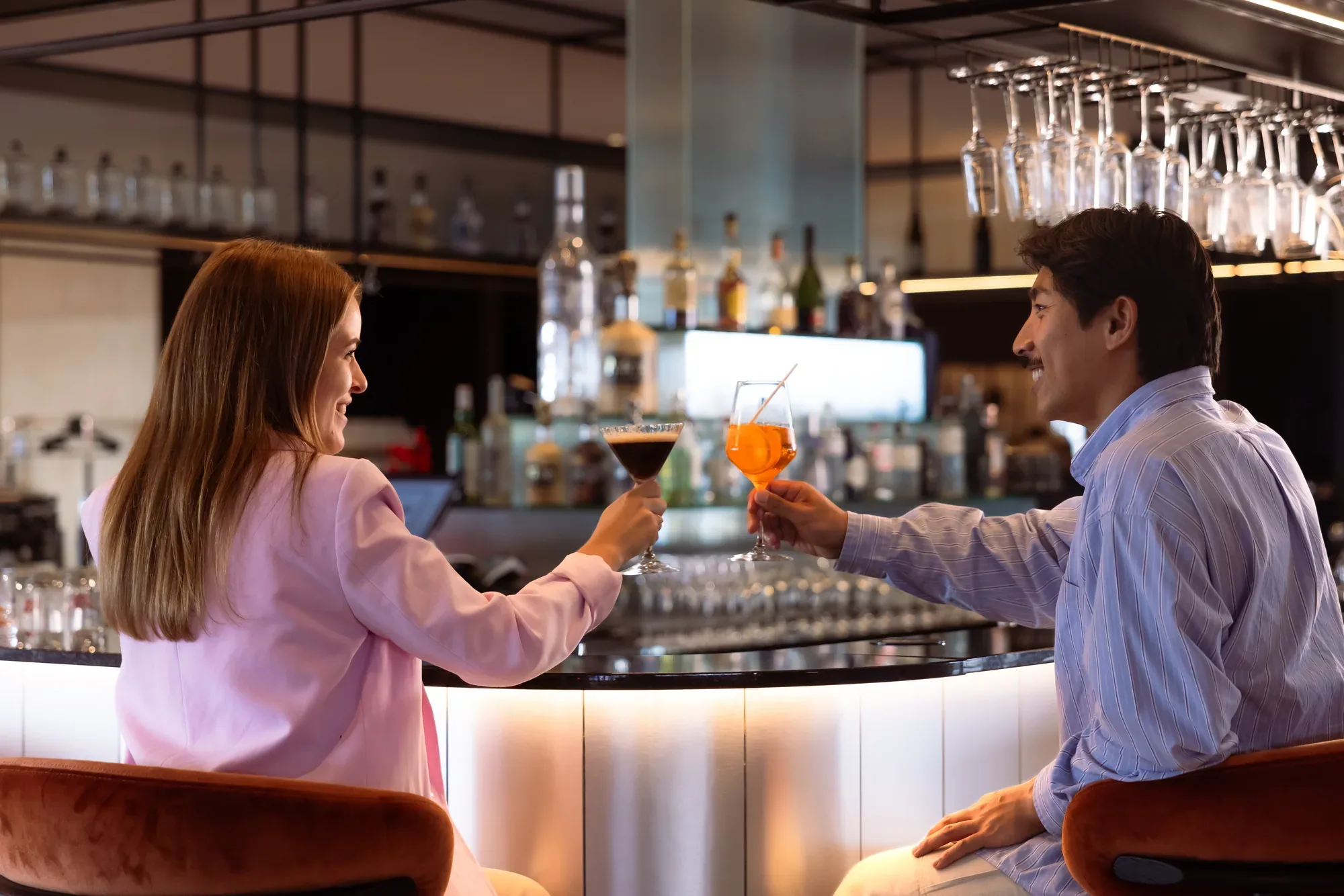 Zwei Gäste stoßen an der beleuchteten Bar des The Passenger Hotel mit Cocktails an