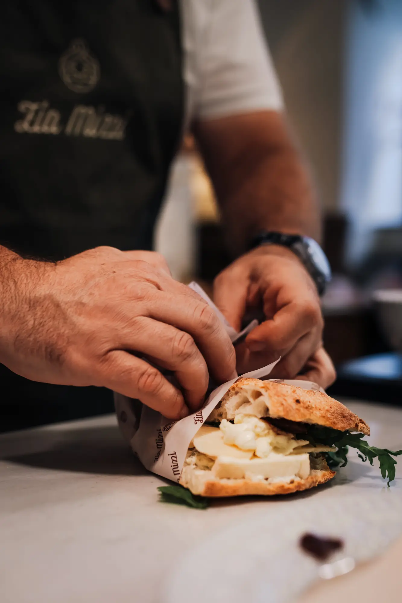Hände in Zia-Mizzi-Schürze wickeln eine Focaccia in Papier