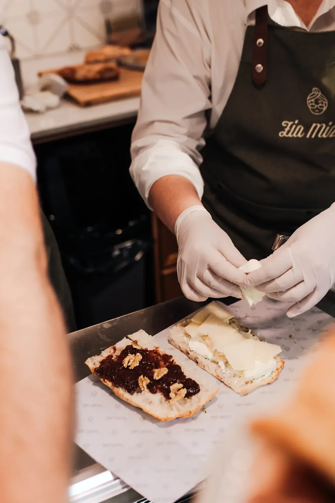 Mitarbeiter mit Zia-Mizzi-Schürze belegt Brote mit Käse und Walnüssen an der Theke