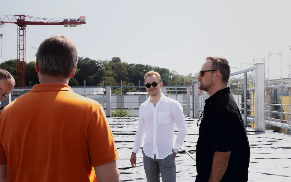 Gespräch mit Kunden auf dem Dach einer Baustelle, im Hintergrund ein Kran