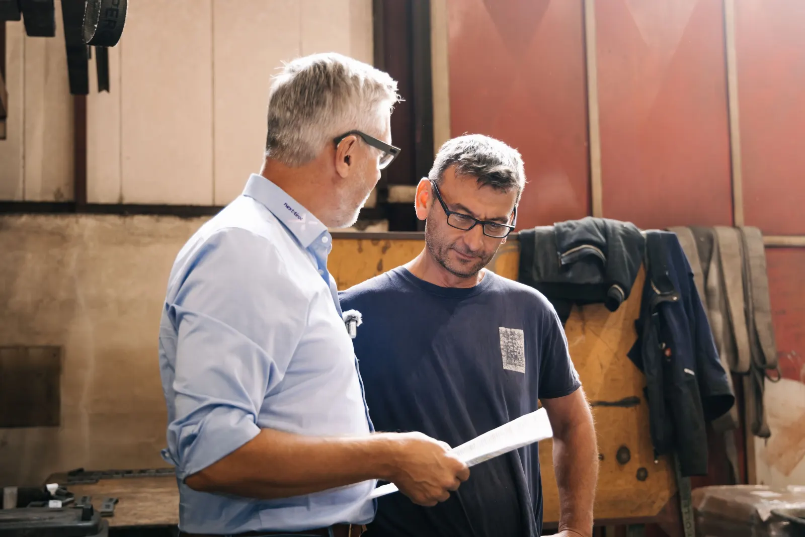 Zwei Männer besprechen in einer Werkstatt einen Arbeitsauftrag auf Papier