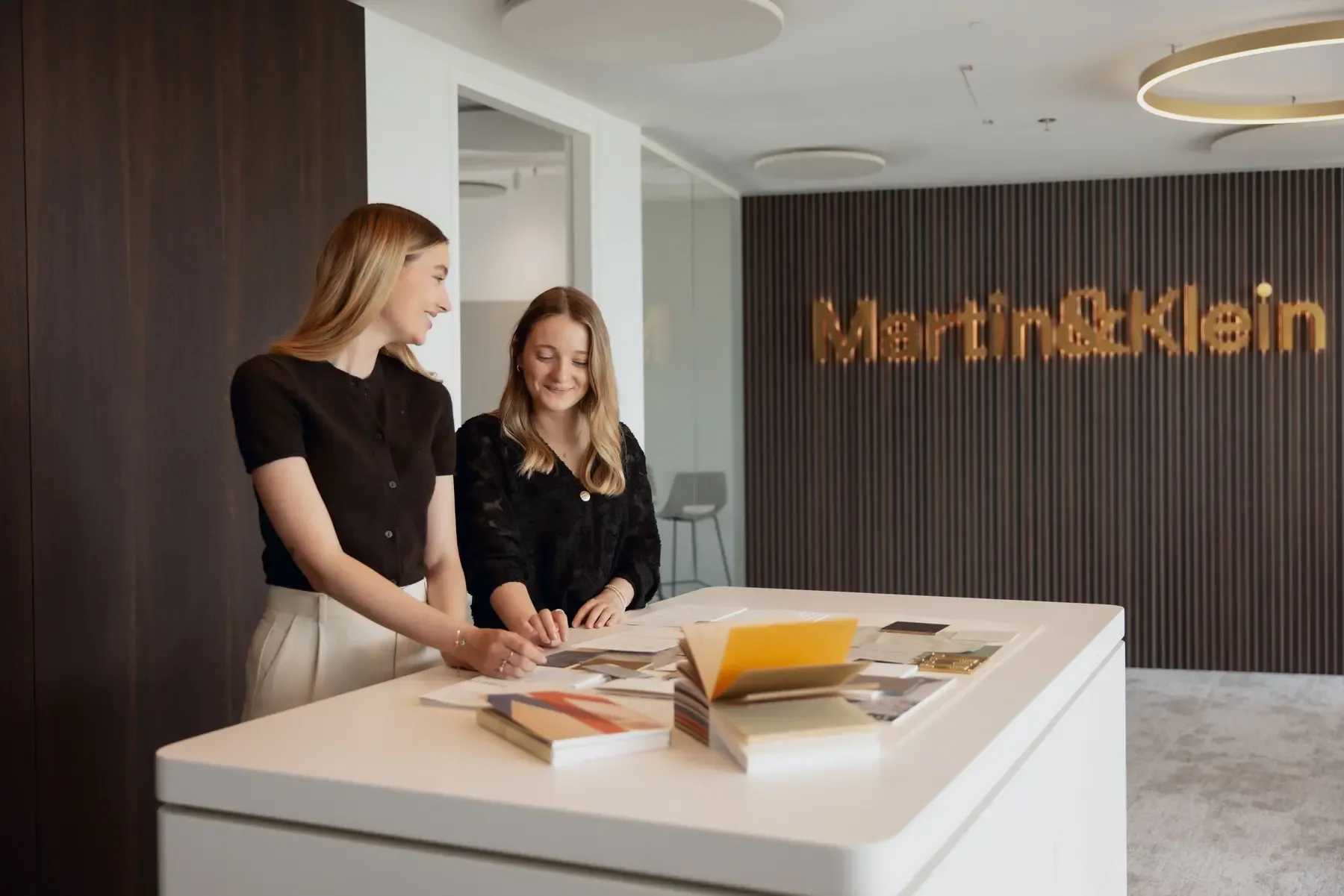 Zwei Kolleginnen von Martin&Klein arbeiten vor der Logo-Wand im Büro im Helix