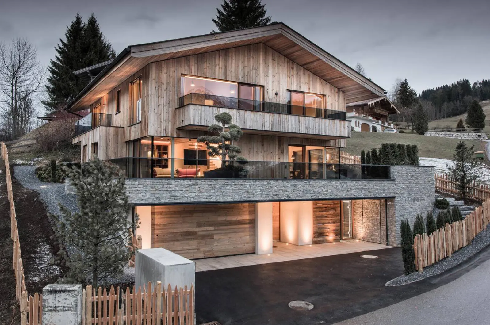 Wohnhaus mit Holzfassade und Satteldach, in der Abenddämmerung beleuchtet