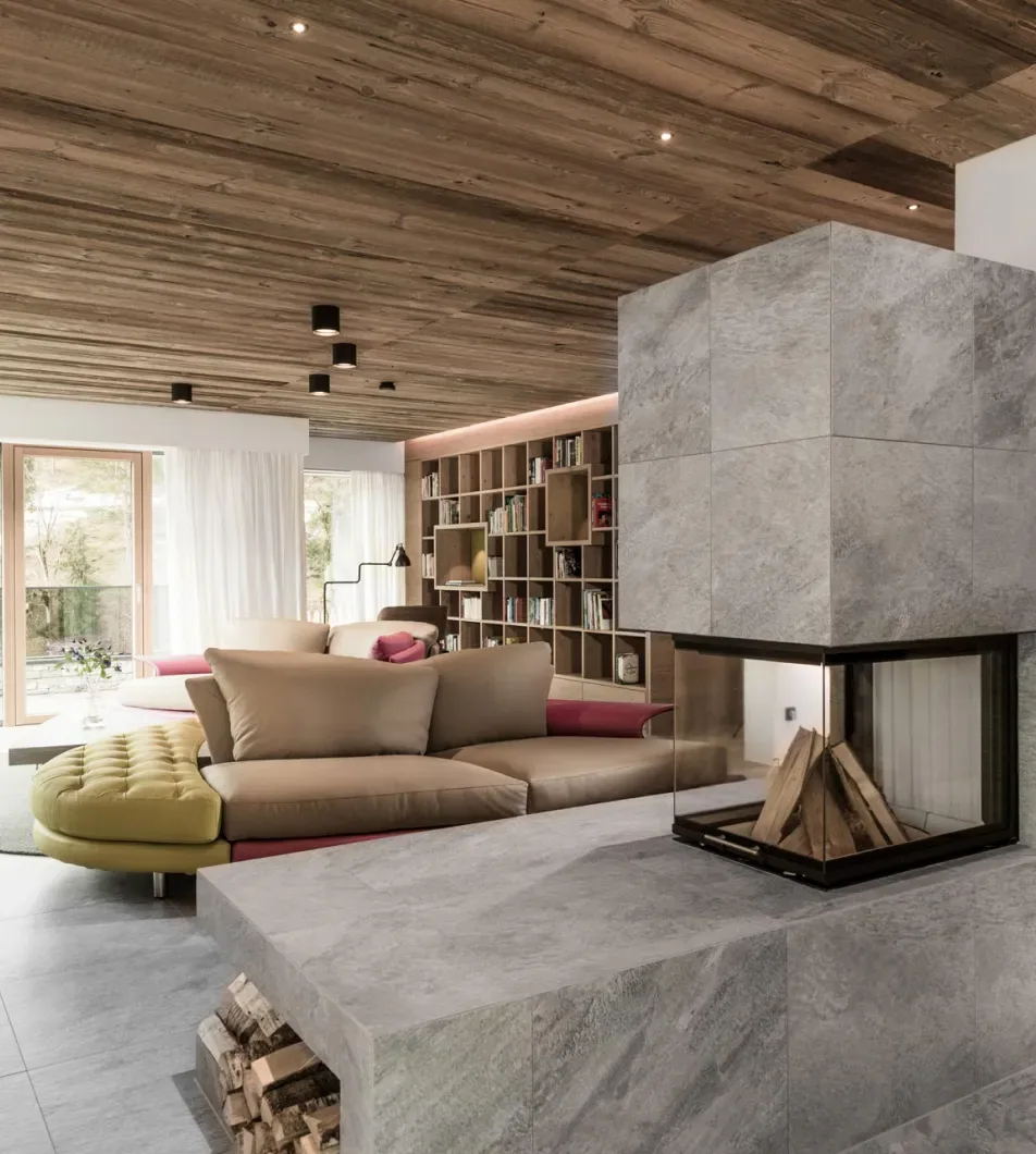 Wohnraum mit freistehendem Kamin aus Sichtbeton, Holzdecke und eingebauter Bücherwand