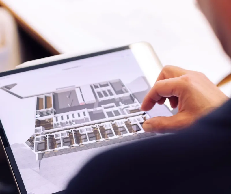 Hand zeigt auf ein Tablet mit dem 3D-Modell einer Wohnanlage
