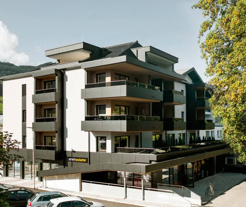 Mehrgeschossiges Wohn- und Geschäftshaus mit umlaufenden Balkonen und dunklen Holzelementen
